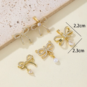 Golden bow pendants with micro-set zircons, pearls and heart drops on stone surface