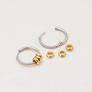 Detail of silver hoop earrings with white zircon stones and gold bead charms
