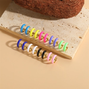 Colorful enamel C-shaped hoop earrings in gold metal finish displayed on travertine