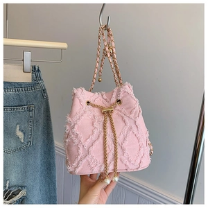 Pink denim bucket bag with frayed edges and pearl drawstring detailing on golden chain