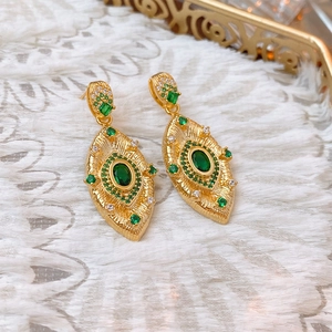 Detailed close-up of vintage gold leaf earrings with green and white gemstones