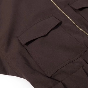 Detail of dark brown utility jacket featuring large flap pocket and metal zipper closure