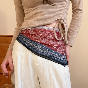 Detail of red paisley silk scarf used as a stylish waist belt on beige knitwear
