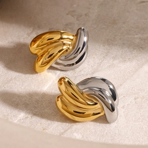 Minimalist twisted gold and silver hoop earrings on a light beige textured stone base