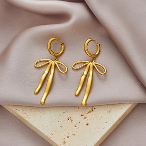 Detail of golden bow-shaped stainless steel earrings on elegant fabric and stone