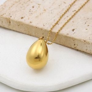 Close-up of a sleek gold teardrop necklace pendant resting on a textured stone tray