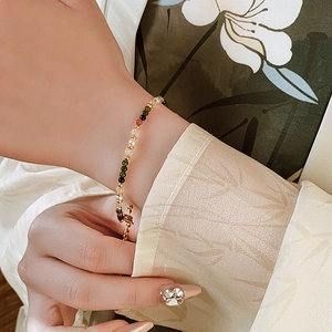 Close-up of 18K gold plated beaded bracelet with green and red stones on a model's wrist