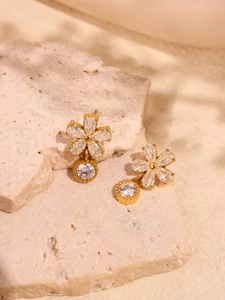 Vue macro de boucles d'oreilles fleur dorées avec zircon 5A sur socle en travertin