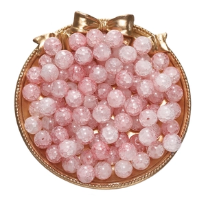 Macro shot of pink cracked glass beads for DIY jewelry making in a golden bow tray