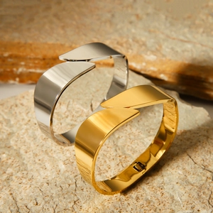 Polished gold and silver stainless steel open bangles on a textured stone surface