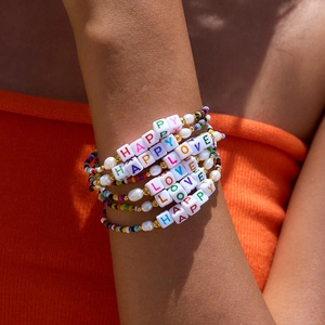 Macro detail of stacked colorful resin bead bracelets with LOVE and HAPPY letter charms