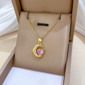 Detail of a gold crescent moon pendant with a pink heart gemstone in a brown jewelry box