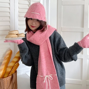 Detail view of pink knit winter set featuring hat and scarf with white tie accents