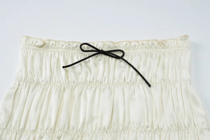 Detail of cream satin skirt featuring elastic pleated waist and black ribbon bow tie