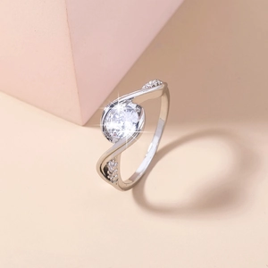 Detailed close-up of a silver ring with a round clear gemstone on a soft peach background