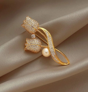 Close-up of golden tulip brooch with sparkling zircons and pearl on silk fabric