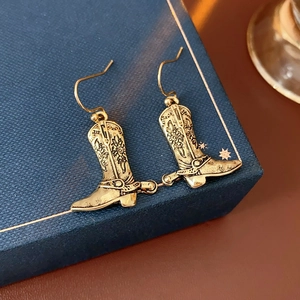Vue détaillée de boucles d'oreilles bottes de cowboy dorées vintage sur un coffret