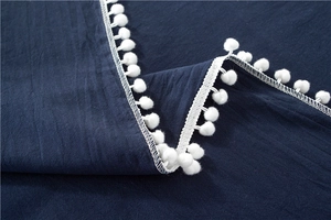 Close-up of deep blue cotton tablecloth with decorative white pom-pom fringe details
