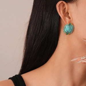 Vue macro de boucles d'oreilles turquoise avec strass bleus et monture dorée sur modèle