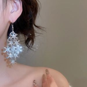 Close-up of sparkling silver snowflake tassel earrings with rhinestones on a model