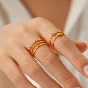 Close-up of stacked gold stainless steel rings with beaded textures and floral accents