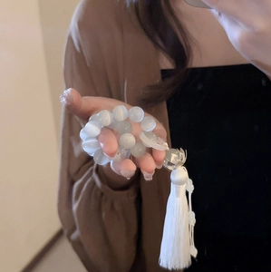 Detail of white cat-eye stone bead bracelet with silk tassel and floral metal charm