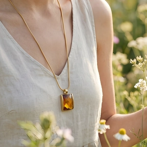 Detailed view of amber glass pendant on 18K gold plated snake chain necklace worn by model