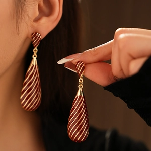 Détail de boucles d'oreilles vintage en émail bordeaux avec rayures dorées
