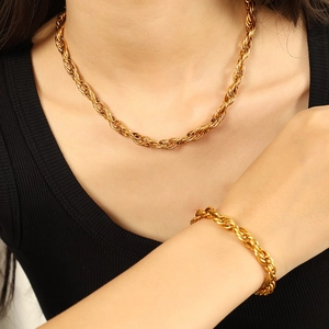 Elegant gold twist chain necklace and bracelet set worn by a model over a black ribbed top