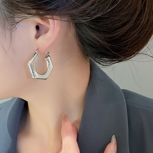 Close-up detail of geometric hexagonal hoop earring in polished silver on a female model