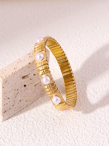 Dettaglio di un bracciale elastico dorato con perle d'acqua dolce su base in pietra