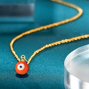 Macro view of an orange evil eye charm pendant on a fine golden necklace chain