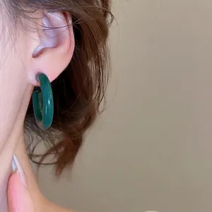Boucles d'oreilles créoles épaisses en acrylique vert foncé portées par un modèle