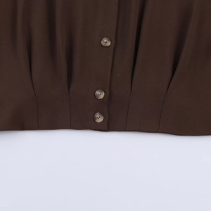 Gros plan sur l'ourlet avant avec de petits boutons ronds sur une chemise marron foncé