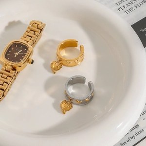 Detail of adjustable heart charm rings and gold watch displayed on a ceramic tray