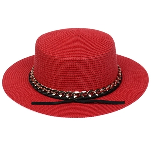 Close-up of red straw sun hat featuring a black ribbon and gold metal chain detail