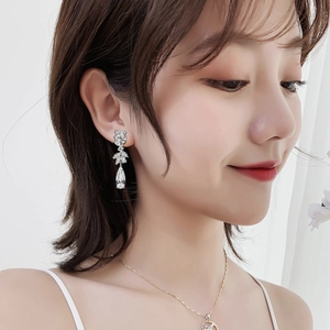 Macro detail of silver drop earrings with leaf-shaped studs and crystal teardrops