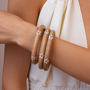 Close-up of three wooden bangles with white daisy floral prints worn on a wrist