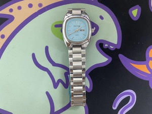 Detail of silver stainless steel square watch showing light blue dial and day-date window