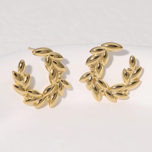 Macro shot of gold laurel leaf stud earrings in stainless steel on white background