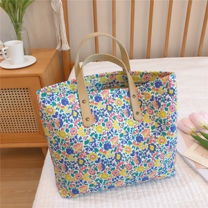 Floral fabric tote bag with cream leather handles and gold studs on a cozy bed