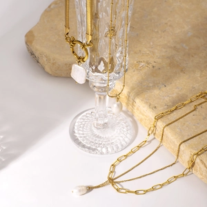 Collier multicouches en acier doré avec perles naturelles drapé sur un verre élégant