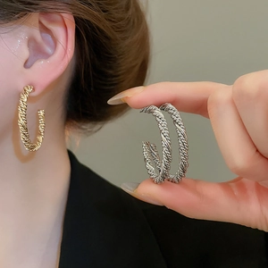 Macro view of C-shaped twisted rope earrings in polished gold and silver metal finish