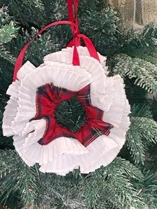 Detail of a ruffled plaid scrunchie with red ribbon hanging on a snowy Christmas tree