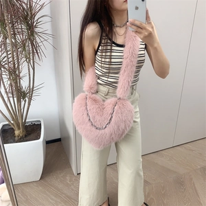 Pink heart-shaped plush crossbody bag with metal chain detail shown on a model