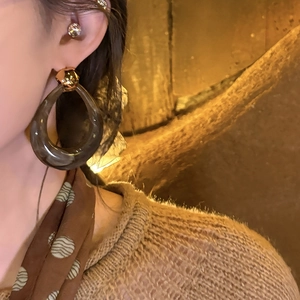 Close-up of a model wearing dark amber resin hollow hoop earrings with gold details