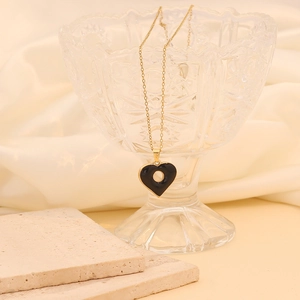 Collier en chaîne dorée avec pendentif cœur noir exposé sur le rebord d'un verre