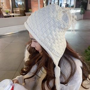Detail of white chunky knit earflap hat featuring long tassels and warm braided texture