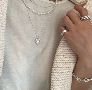 Close-up of minimalist silver heart necklace, pearl jewelry, and star rings on a model