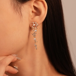 Elegant gold drop earrings with zircon and pearls worn by a model in a close-up profile shot
